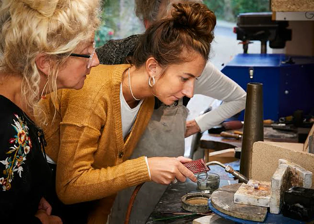 Two jewellers at the bench, one soldering a setting under a torch